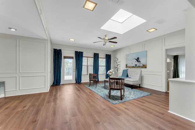 living area with a skylight, visible vents, ceiling fan, wood finished floors, and a decorative wall