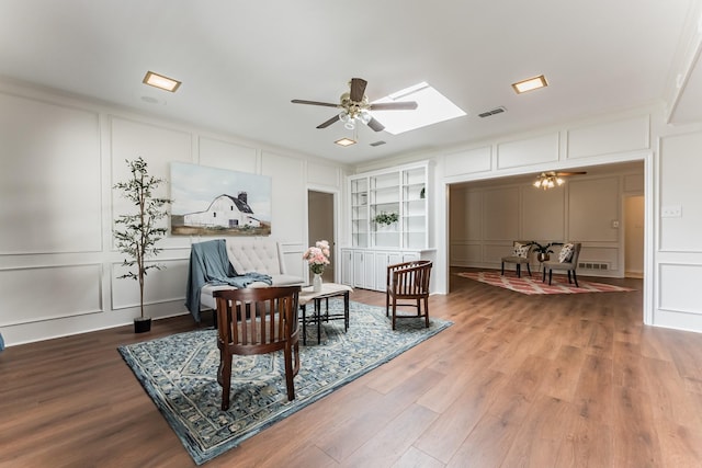 living area featuring visible vents, built in shelves, a ceiling fan, and a decorative wall