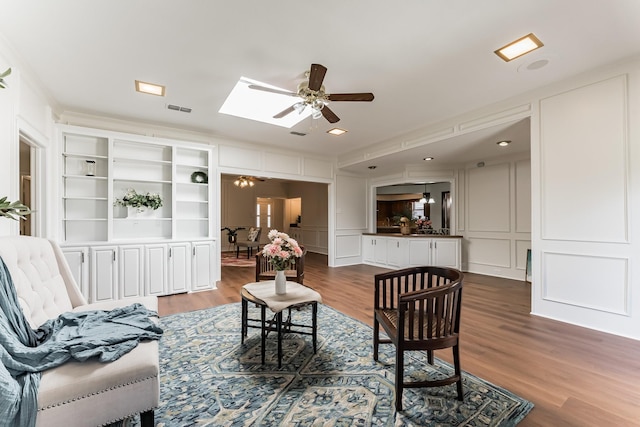 living area with a skylight, visible vents, a decorative wall, ceiling fan, and wood finished floors