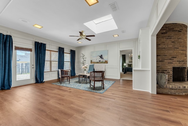 sitting room featuring a skylight, a decorative wall, and light wood finished floors