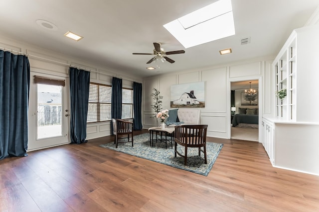 living area featuring light wood-style floors, a skylight, visible vents, and a decorative wall