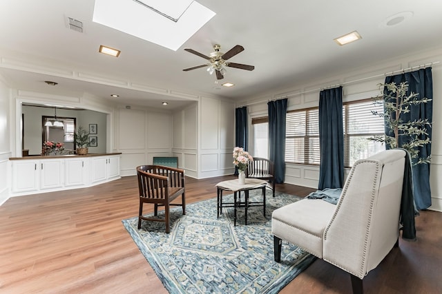 living room with light wood-style floors, a skylight, visible vents, and a decorative wall