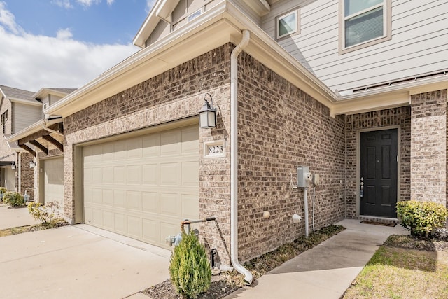 doorway to property featuring an attached garage, driveway, and brick siding