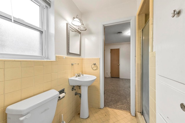 bathroom with a healthy amount of sunlight, a shower stall, tile walls, and wainscoting