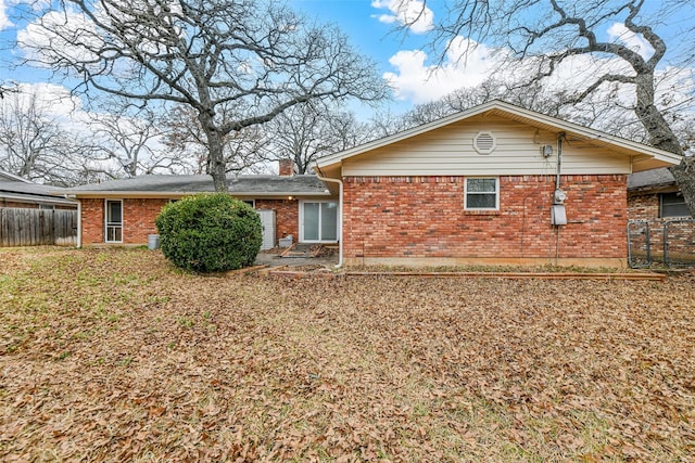 rear view of property featuring brick siding, a chimney, and fence