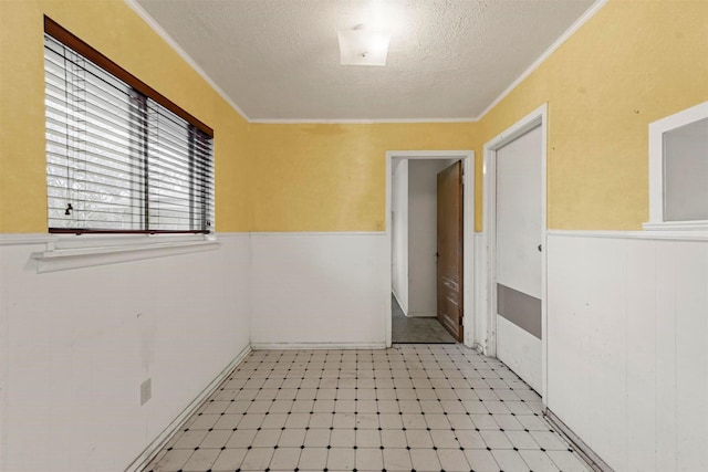 empty room with ornamental molding, a wainscoted wall, a textured ceiling, and light floors