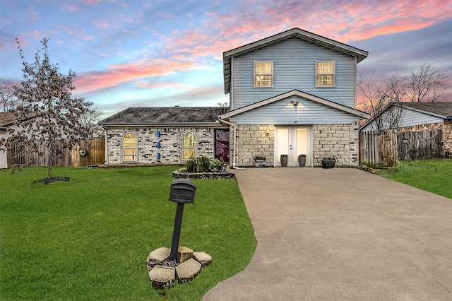 traditional-style home with stone siding, fence, concrete driveway, and a yard