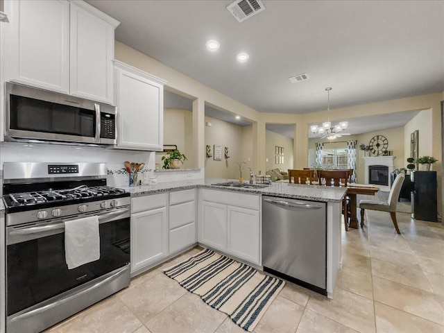 kitchen with stainless steel appliances, visible vents, white cabinets, a sink, and a peninsula