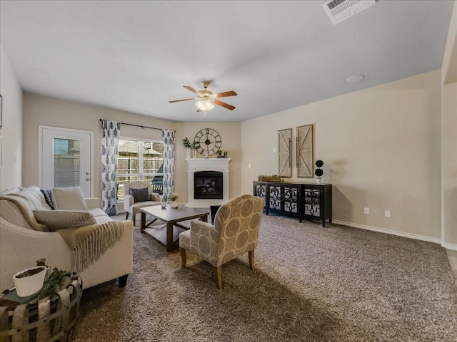 carpeted living room with baseboards, visible vents, a ceiling fan, and a glass covered fireplace