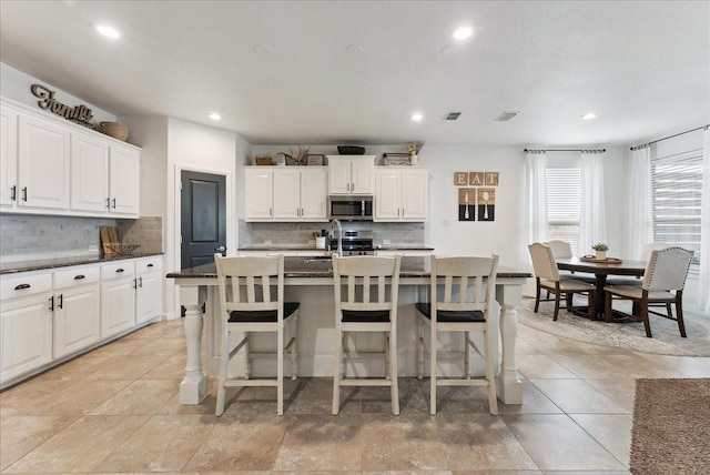 kitchen with a breakfast bar area, a kitchen island with sink, visible vents, decorative backsplash, and stainless steel microwave