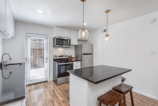 kitchen featuring white cabinets, dark countertops, appliances with stainless steel finishes, light wood-type flooring, and a sink