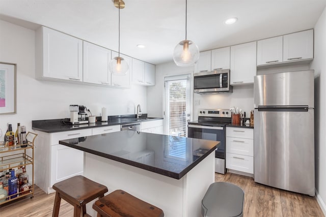 kitchen featuring dark countertops, appliances with stainless steel finishes, white cabinets, light wood-type flooring, and a kitchen bar