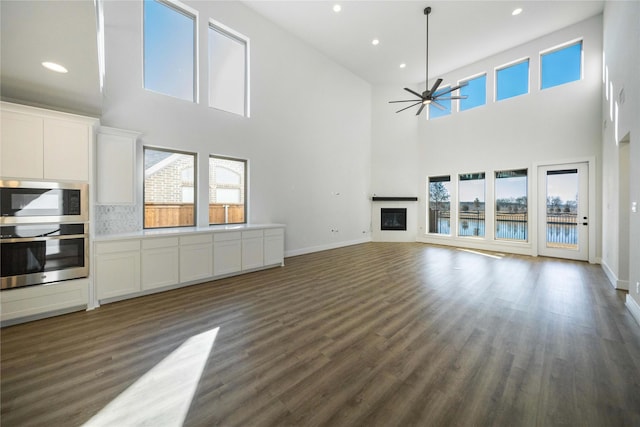 unfurnished living room featuring dark wood finished floors, recessed lighting, a glass covered fireplace, ceiling fan, and baseboards