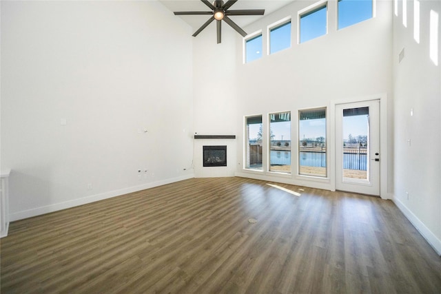 unfurnished living room featuring a wealth of natural light, a glass covered fireplace, baseboards, and wood finished floors