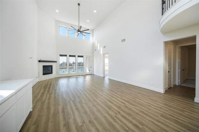 unfurnished living room with a glass covered fireplace, visible vents, ceiling fan, and light wood finished floors