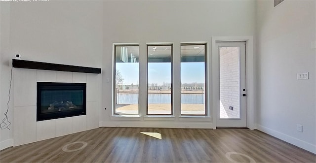 unfurnished living room featuring a tile fireplace, a water view, wood finished floors, and baseboards