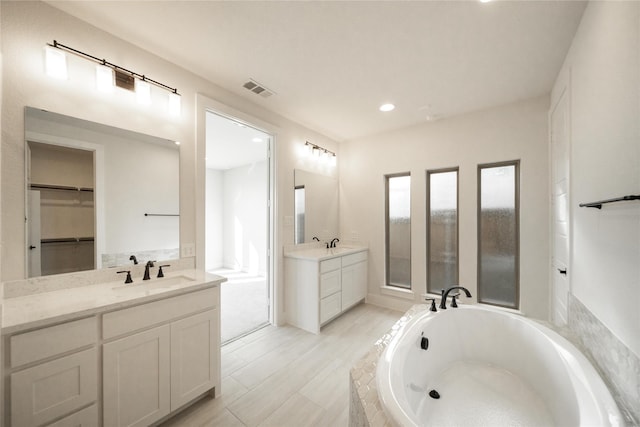 full bath featuring visible vents, a sink, a garden tub, a spacious closet, and two vanities