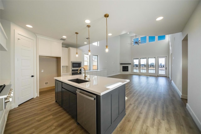 kitchen featuring a center island with sink, stainless steel appliances, white cabinets, a sink, and wood finished floors