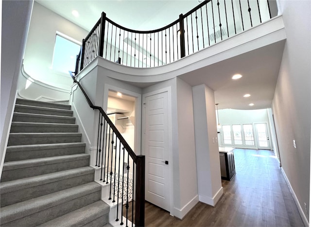 stairs featuring recessed lighting, baseboards, a high ceiling, and wood finished floors