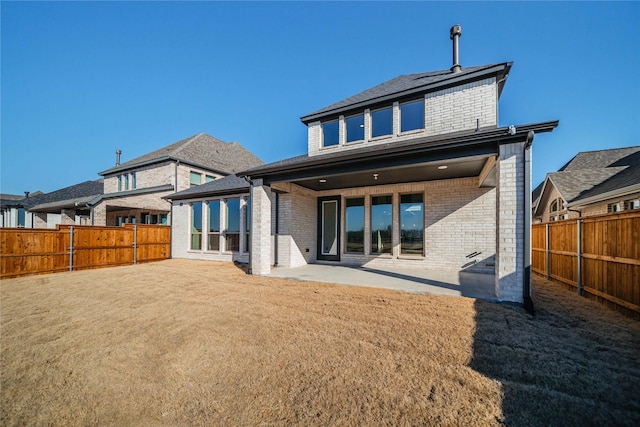 back of property with brick siding, a patio, a fenced backyard, and a lawn