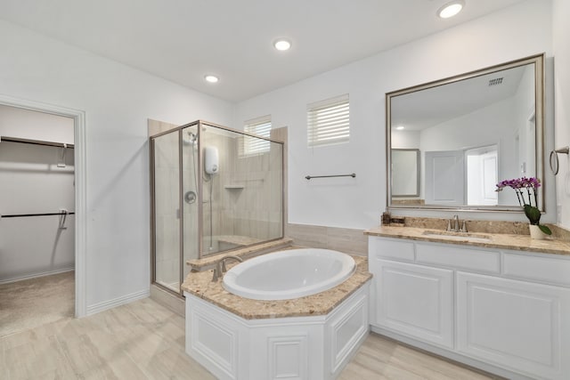 bathroom with a walk in closet, a garden tub, a stall shower, recessed lighting, and vanity