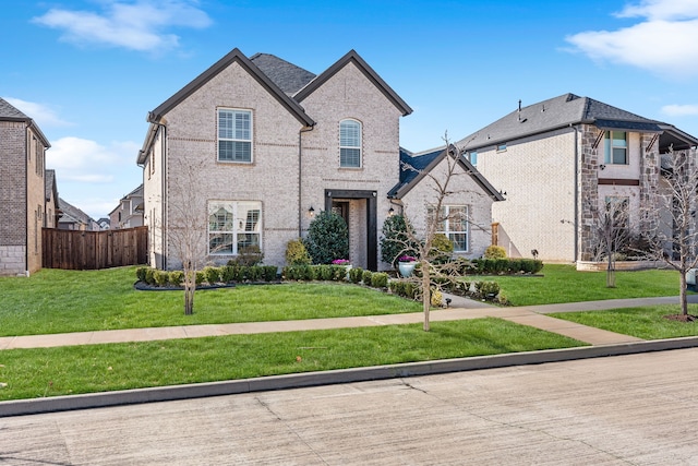 french country inspired facade with brick siding, a front yard, and fence