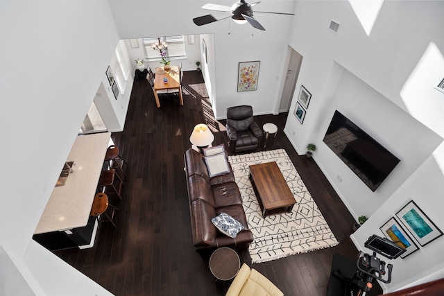 living room featuring hardwood / wood-style floors, visible vents, baseboards, a high ceiling, and ceiling fan with notable chandelier