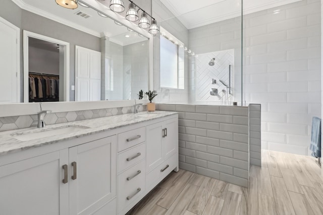 bathroom featuring a walk in shower, a sink, visible vents, tile walls, and ornamental molding