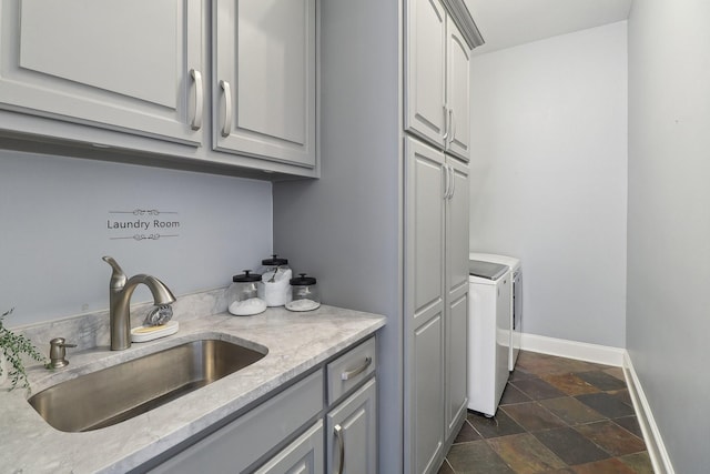 laundry room with cabinet space, baseboards, independent washer and dryer, stone tile flooring, and a sink