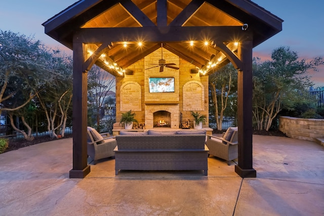 patio terrace at dusk with ceiling fan and an outdoor living space with a fireplace