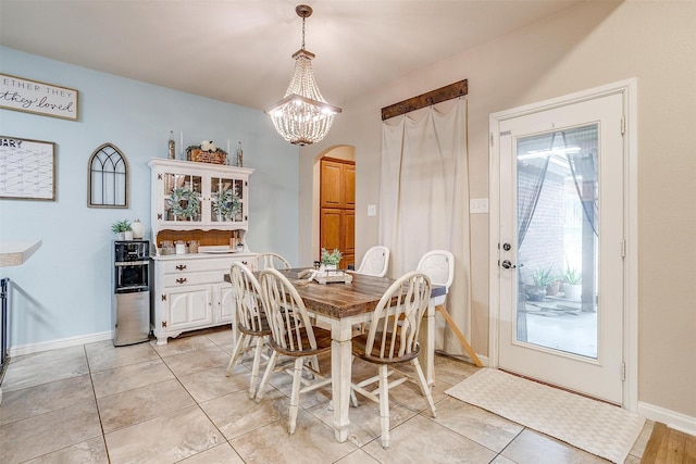 dining area featuring an inviting chandelier, baseboards, light tile patterned floors, and arched walkways