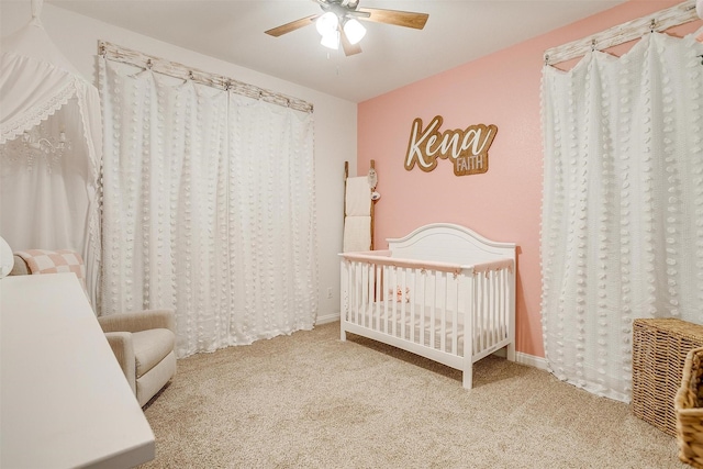 carpeted bedroom with a crib and ceiling fan