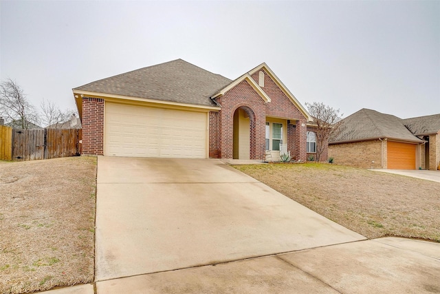 traditional-style home featuring driveway, a garage, a shingled roof, fence, and brick siding