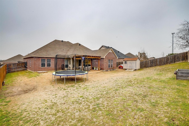 rear view of house with an outbuilding, brick siding, a lawn, a storage unit, and a trampoline