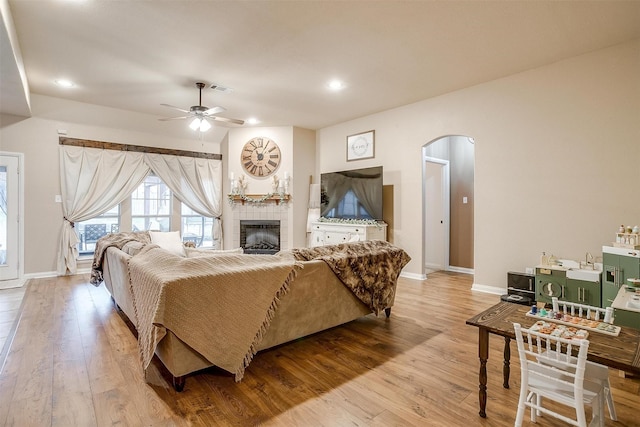 living room with arched walkways, ceiling fan, light wood finished floors, and a fireplace