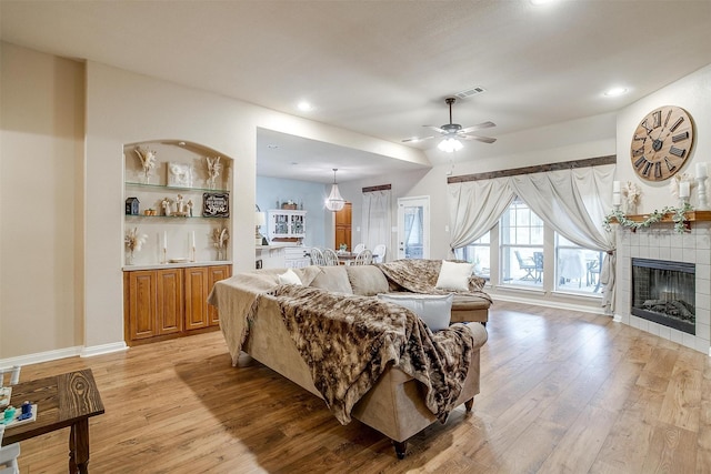 living room with light wood finished floors, visible vents, a ceiling fan, and a tile fireplace