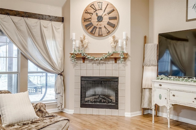 living room with baseboards, a tiled fireplace, and wood finished floors