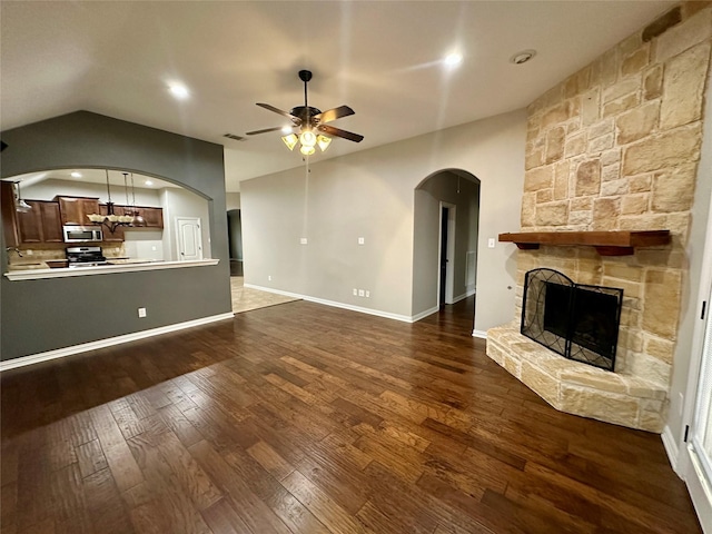 unfurnished living room with a fireplace, lofted ceiling, visible vents, dark wood-type flooring, and ceiling fan