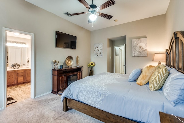 bedroom with baseboards, light colored carpet, ceiling fan, and ensuite bath