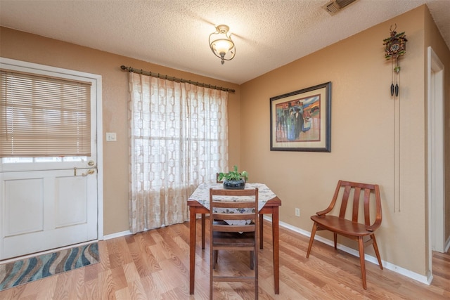 dining room featuring visible vents, a textured ceiling, light wood-style flooring, and baseboards