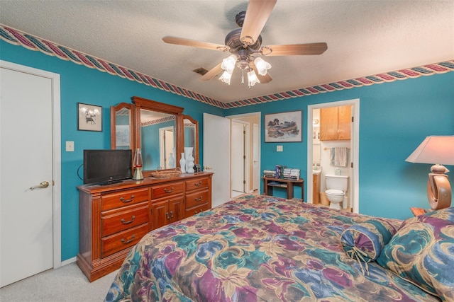 bedroom featuring light carpet, visible vents, ceiling fan, ensuite bathroom, and a textured ceiling