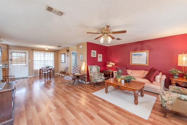 living room with light wood-type flooring, ceiling fan, visible vents, and a textured ceiling