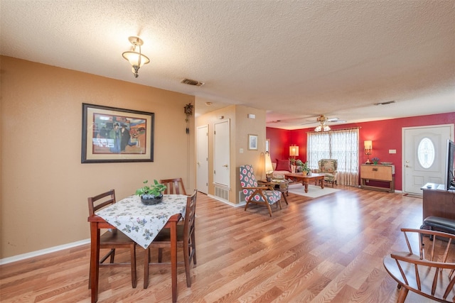 dining space with light wood-type flooring, visible vents, and a textured ceiling