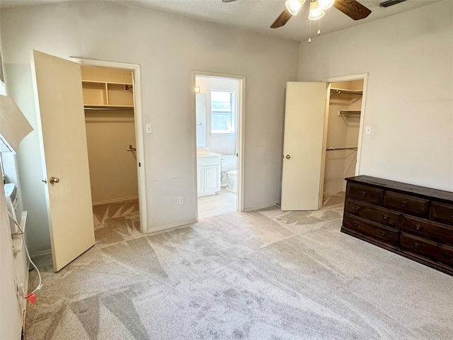 bedroom featuring ensuite bathroom, light colored carpet, a ceiling fan, a spacious closet, and a closet