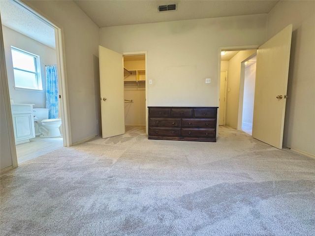 unfurnished bedroom with light carpet, visible vents, a spacious closet, a closet, and ensuite bath