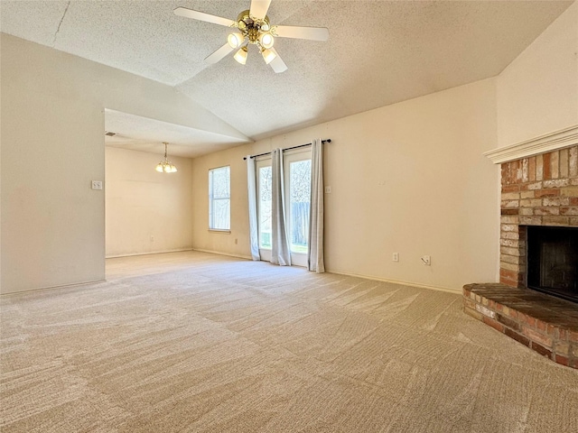 unfurnished living room with a textured ceiling, ceiling fan with notable chandelier, carpet flooring, vaulted ceiling, and a brick fireplace