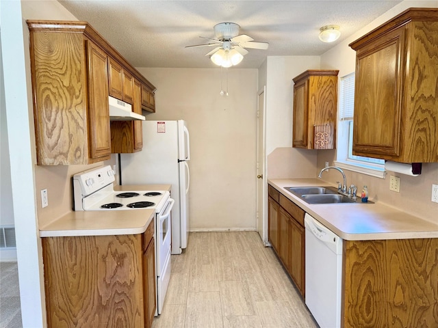 kitchen featuring white appliances, brown cabinetry, a sink, and under cabinet range hood