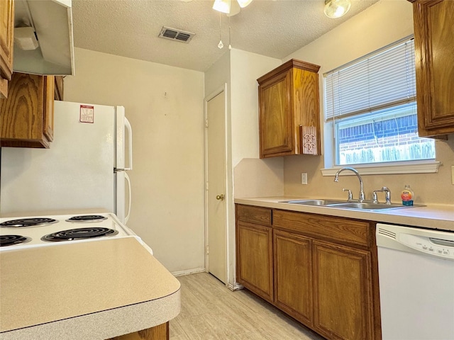 kitchen with white appliances, visible vents, brown cabinets, light countertops, and a sink