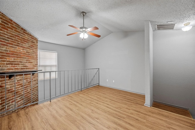 empty room with lofted ceiling, a textured ceiling, visible vents, and wood finished floors