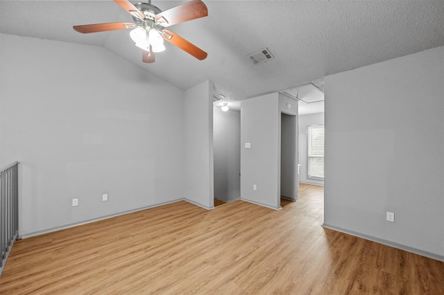 empty room featuring light wood finished floors, attic access, visible vents, lofted ceiling, and a textured ceiling